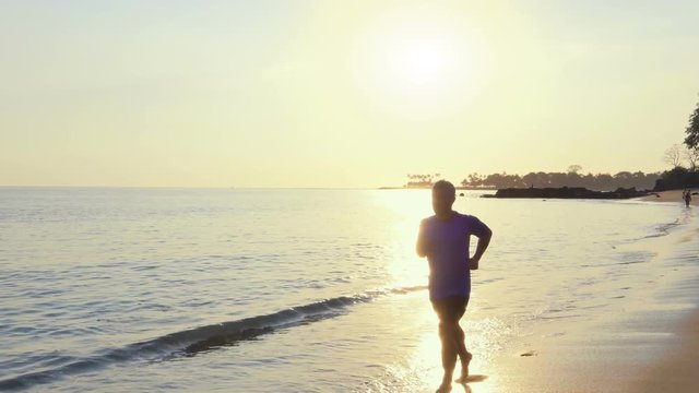 athletic fit male  runs at the beach jogging training exercise work out for marathon sunset steadycam shot  tracking