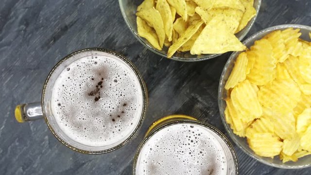 A glass with beer and snacks on a plate on a dark table. A plate of potato chips to beer. Top view of beer and snacks rotation 360