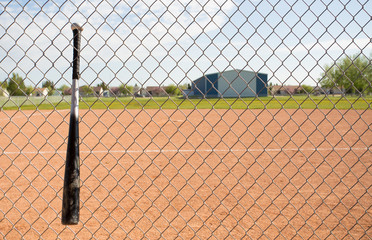 A baseball hat hanging from a wire fence in front of a blurred baseball field