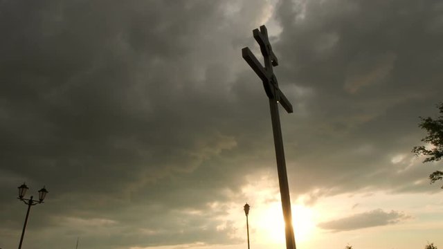 A large cross silhouetted against storm clouds at sunset.