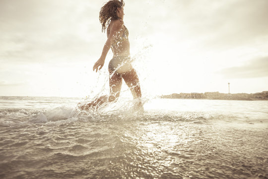 Spain, Tenerifa, young woman running into water against the sun