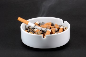 White ceramic ashtray full of smokes cigarettes. Selective focus.