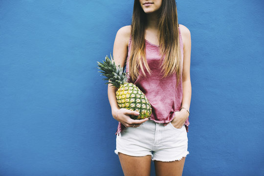 Young woman standing with pineapple at blue wall