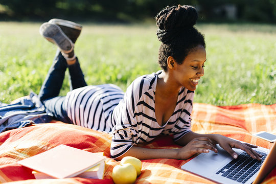 Young woman lying on blanket on a meadow using laptop