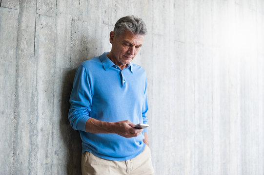 Senior man at concrete wall looking on cell phone
