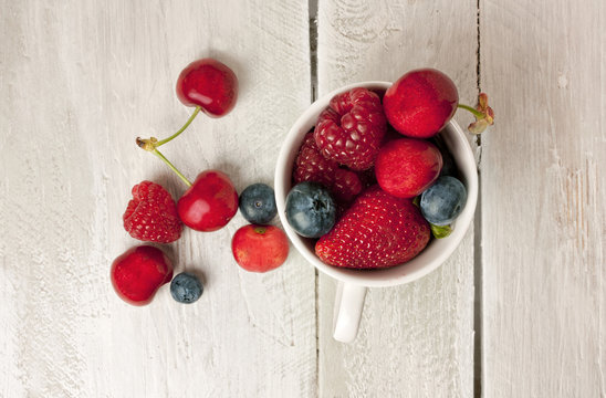 White cup with fresh cherries, strawberries, blueberries and rasspberries