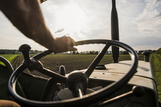 Close-up of farmer steering tractor next to field