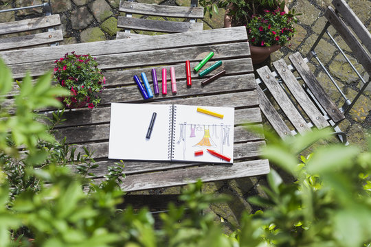 Drawing, sketch book with woman's drawing and coloring pencils on wooden garden table