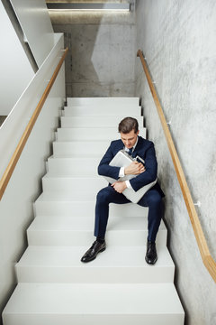 Businessman sitting on stairs clutching his briefcase