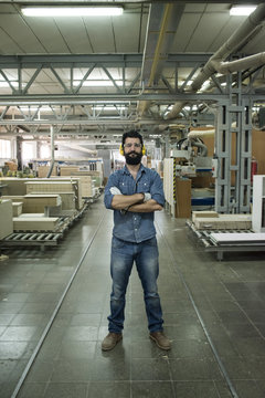 Man with hearing protection, safety glasses and gloves smiling with his arms crossed in a factory