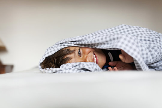 Smiling little boy lying under the blanket on his bed