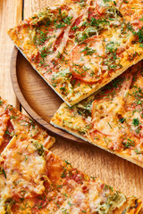 Slices of a traditional pizza with ham, cheese and tomatoes sprinkled with herbs on wooden plate
