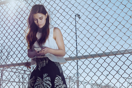 Attractive young woman at a fence texting on cell phone