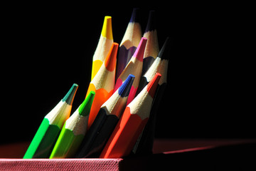 2 Kolorowe kredki stojące w czerwonym pudełku. Zbliżenie na pomieszane kredki na czarnym tle z bocznym oświetleniem. © polmus