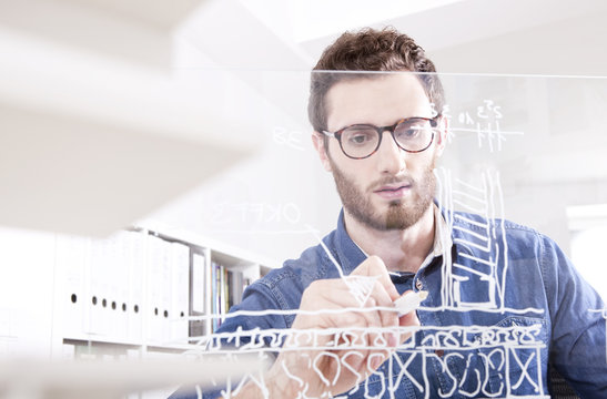 Portrait of young man drawing on glass pane in an office