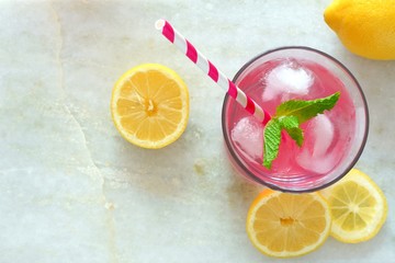 Glass of pink lemonade with mint and lemon slices overhead view on a white marble background