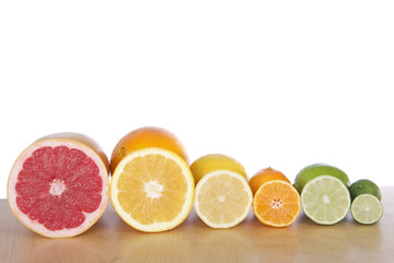 Colorful sliced citrus lined up in rows on a light brown wood table with a white background. Grapefruit, naval orange, lemon, lime, cuties clementine and a key lime