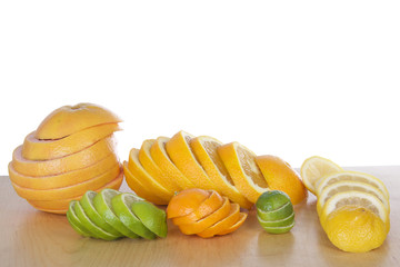 Colorful sliced citrus lined up in stacks on light brown wood table with a white background....