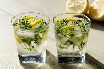 Two glasses of lemonade with thyme, lemon and ice