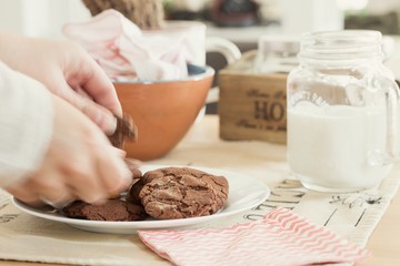 Hands breaking a homemade chocolate cookie over the dining table to take a snack