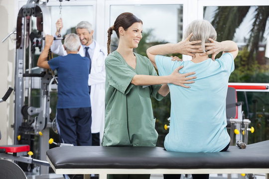 Nurse Assisting Senior Woman In Back Exercise In Rehab Center