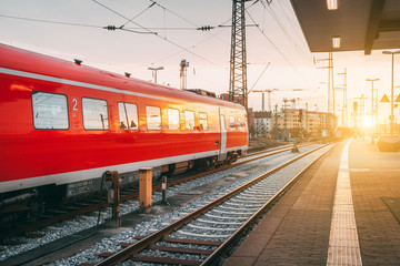 Naklejka premium Beautiful railway station with modern red commuter train at colorful sunset in Nuremberg, Germany. Railroad with vintage toning