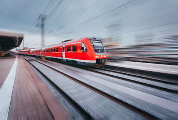 Fototapeta premium Railway station with modern high speed red passenger train at sunset in Nuremberg, Germany. Railroad with motion blur effect vintage toning. Industrial landscape