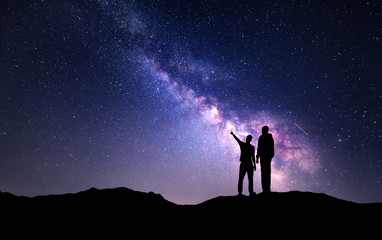 Milky Way with silhouette of a family on the mountain. Father and a son who pointing finger in...