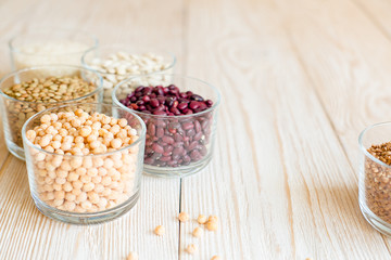 Grain and beans in glass bowls on white wooden background