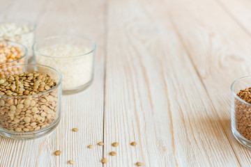 Grain and beans in glass bowls on white wooden background