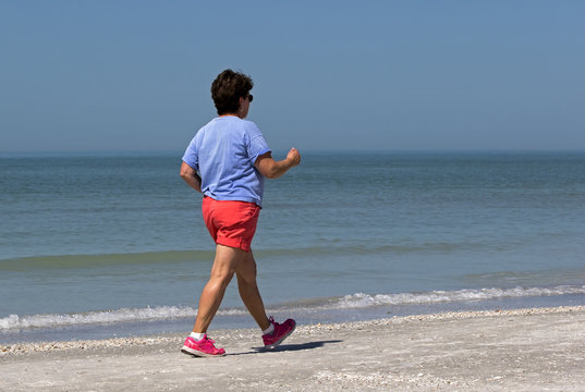 Senior Woman Power Walking On A Gulf Coast Beach.