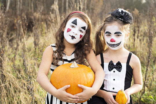 Girls with painted faces holding pumpkins
