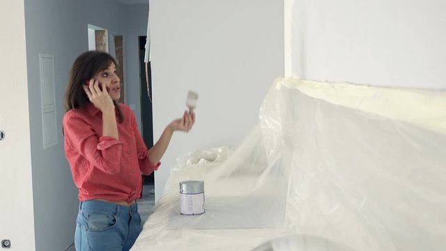 Angry woman talking on cellphone and painting wall in kitchen at her new home
