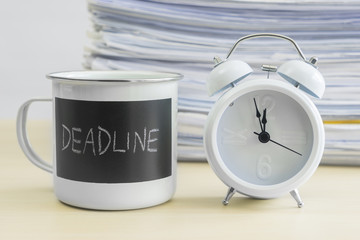 Deadline words on mug with clock and stack of papers