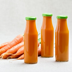 Three bottles of carrot juice with carrots.