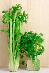 Fresh green celery on brown wooden background near the parsley in a jar of water