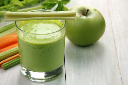 Fresh green celery juice in glass on white wooden background near the carrots and Apple