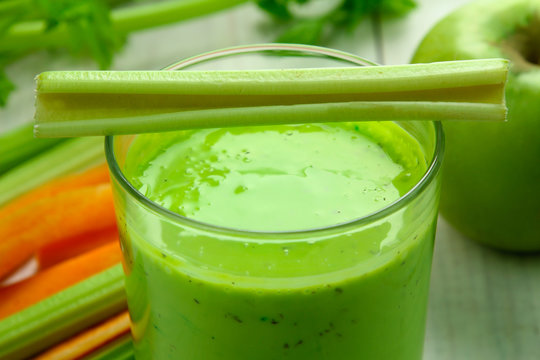 Fresh green celery juice in glass on white wooden background near the carrots and Apple