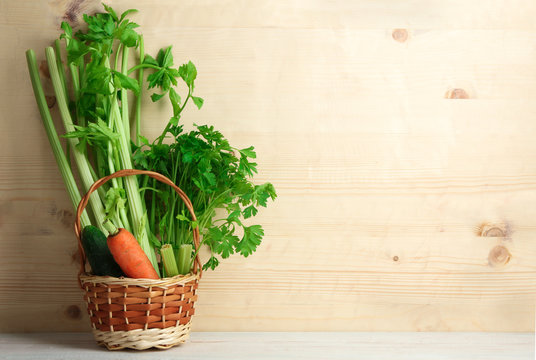 Fresh green celery on brown wooden background in a wicker basket with cucumber and carrots