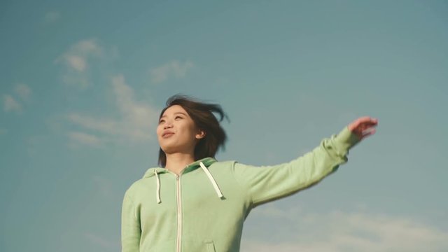 Sensual young asian woman with short hair stretching outdoor. Blue clean sky background