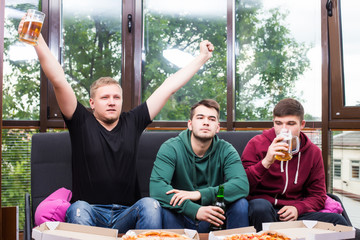Young friends cheering and drinking alcohol while watching soccer match at home