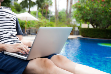 Obraz premium Man using a laptop in the pool on vacation - work anywhere and internet work concept