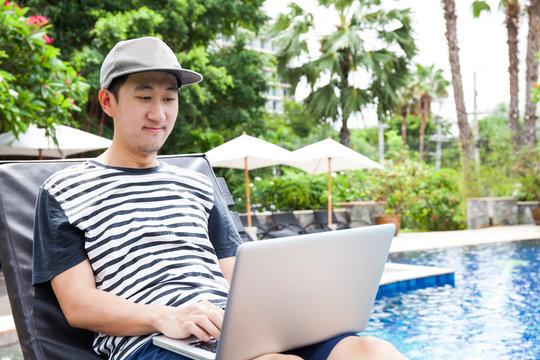 Asian Man Using A Laptop In The Pool On Vacation - Work Anywhere