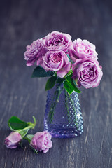 Beautiful fresh purple roses in a vase on a dark brown wooden background .