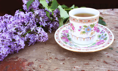 Obraz na płótnie Canvas Tea Cup on a saucer and a branch of lilac in the garden