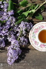 Tea Cup and branch of lilac on wooden background, top view. The tea party outdoors 