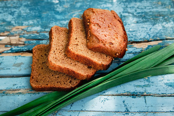 There are Homemade Brad  with Green Fresh Leaves of Garlic on the Vintage Old Panited Wooden Boards,Rural Natural Food,Baking,Top View