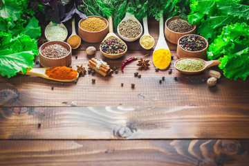 Beautiful colorful spices in wooden spoons and bowls with lettuce, dill and Basil on an old wooden brown table. Free space for your text