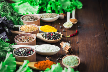 Beautiful colorful spices in wooden spoons and bowls with lettuce, dill and Basil on an old wooden brown table. Free space for your text