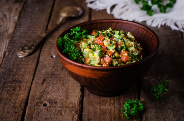 Fresh tabbouleh, a Middle Eastern salad, in clay bowl on wooden background. Selective focus. Toned...